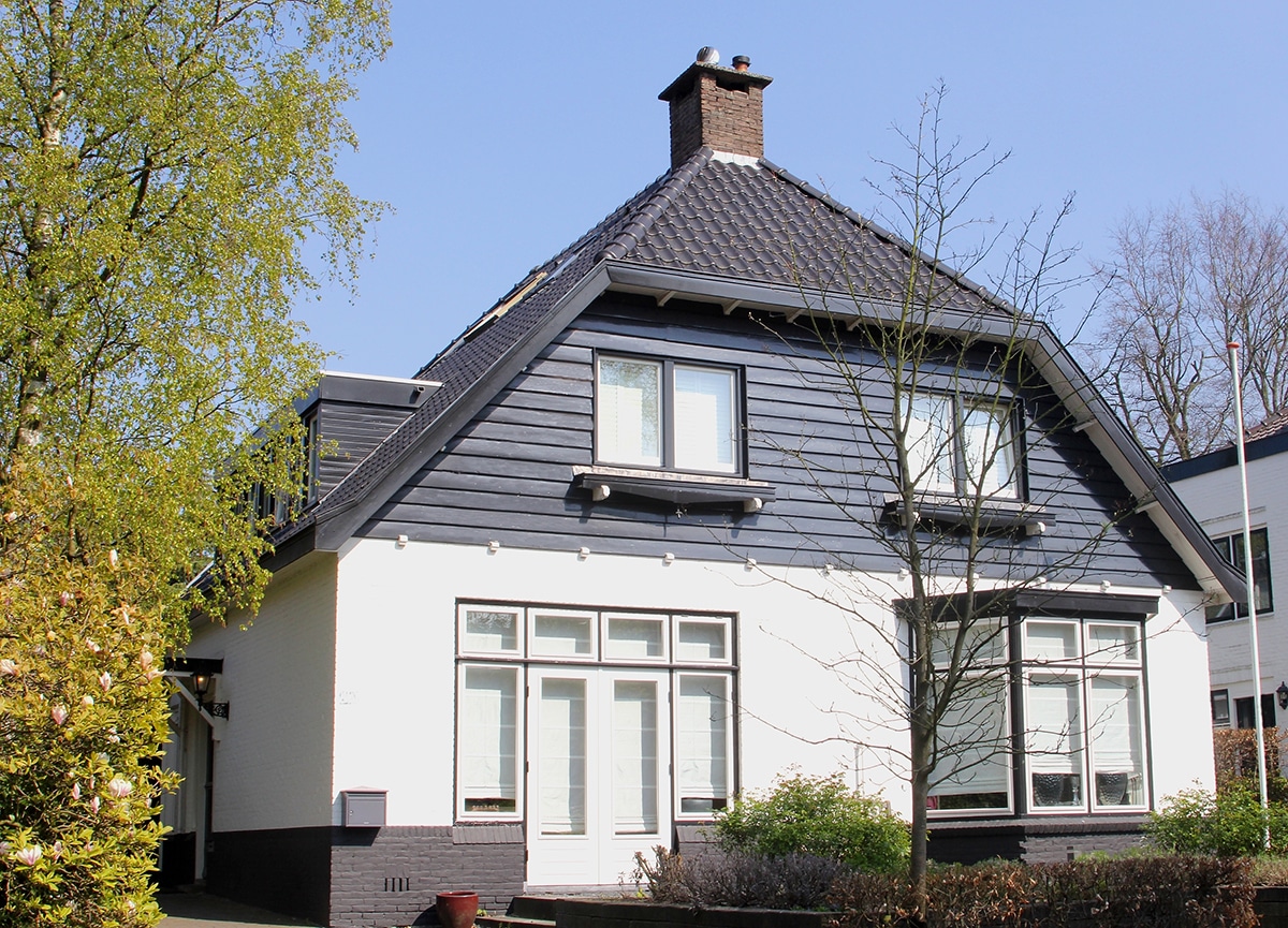 Dutch detached grey house in typical  traditional style with characteristic dormer windows and front garden trees, Holland